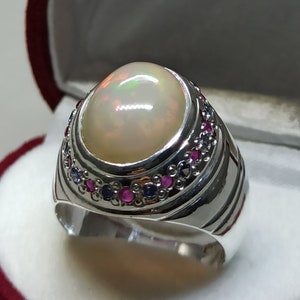May include: A silver ring with a large white opal gemstone surrounded by a band of small pink and blue gemstones.