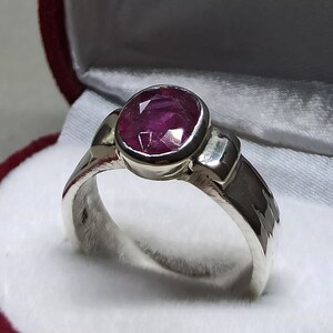 May include: A silver ring with a pink oval gemstone set in a bezel setting. The ring is in a red velvet ring box.