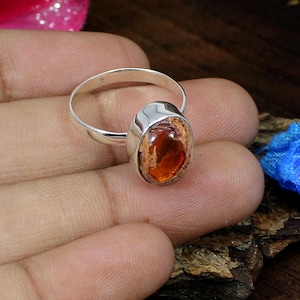 Może przedstawiać: Srebrny pierścionek z owalnym opalem. Opal ma kolor brązowy, pomarańczowy i biały.