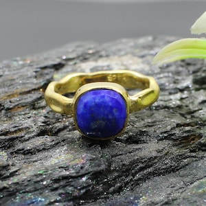 Peut inclure: Une bague en or avec une pierre précieuse en lapis-lazuli bleu. La bague a une bande texturée et une pierre de forme carrée.