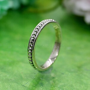 Puede incluir: Un anillo de banda de plata con un borde de cuentas. El anillo es simple y elegante.