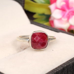 Könnte beinhalten: Ein silberner Ring mit einem roten Edelstein. Der Edelstein ist quadratisch mit einem facettierten Schliff.