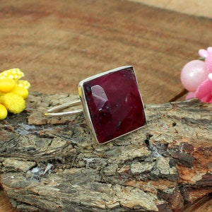 May include: A silver ring with a square, faceted, dark red gemstone.