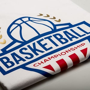 May include: White t-shirt with a blue and gold basketball logo. The logo features a basketball with a blue outline and the word "BASKETBALL" in blue letters. Below the basketball is the word "CHAMPIONSHIP" in red letters.
