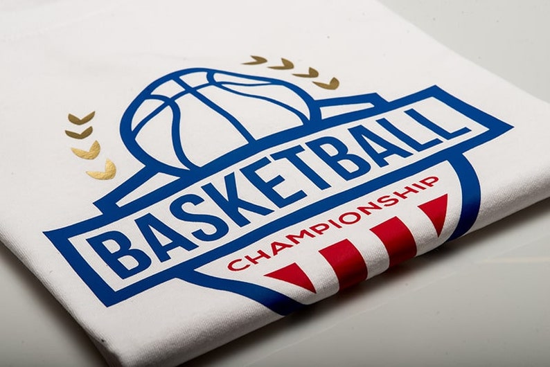 May include: White t-shirt with a blue and gold basketball logo. The logo features a basketball with a blue outline and the word "BASKETBALL" in blue letters. Below the basketball is the word "CHAMPIONSHIP" in red letters.