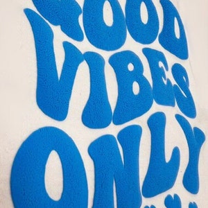 May include: A blue, fuzzy, vinyl-like sticker with the text "Good Vibes Only" in a retro font. The sticker is surrounded by small, blue, fuzzy, flower shapes.