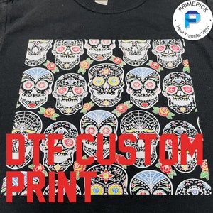 May include: Black t-shirt with a white and colorful sugar skull pattern. The text "DTG CUSTOM PRINT" is printed in red on the front of the shirt.