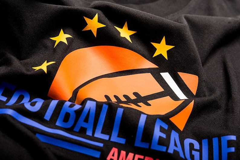 May include: Black t-shirt with a blue and orange graphic of a football and the text "Football League America" with five yellow stars above the football.