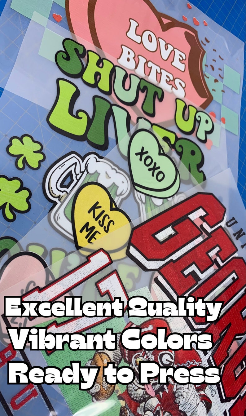 May include: A collection of iron-on heat transfer vinyl designs featuring various phrases and images, including "Love Bites Shut Up Liver", "XOXO", "Kiss Me", and a green shamrock. The designs are ready to be pressed onto fabric.
