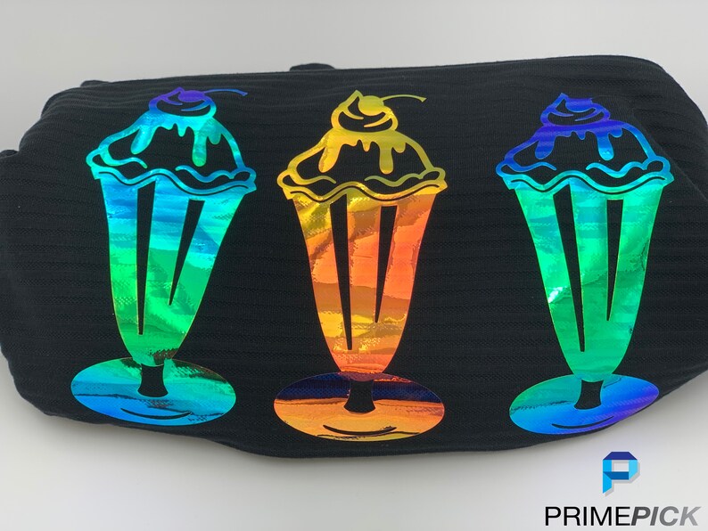 Pu&ograve; includere: Tre disegni di milkshake arcobaleno iridescenti su uno sfondo di tessuto nero. I milkshake hanno una ciliegia in cima e un vortice che cola.