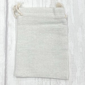 May include: A small, off-white, drawstring pouch made of natural fabric. The pouch is empty and has a simple, rustic look.