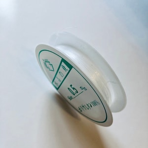May include: A spool of clear 0.5 mm nylon thread. The spool is white with green text that reads "Size 0.5 mm Nylon 100%".