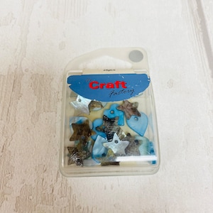 May include: A package of 24pcs of blue and brown shell-like star and heart shaped buttons. The package is labeled "The Craft Factory".