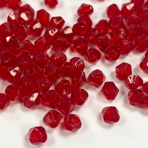 Peut inclure: Des perles de verre facettées rouges éparpillées sur une surface blanche.
