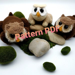Op de afbeelding: Drie gehaakte amigurumi-speelgoed uilen, twee bruin en één wit, met een bruine uil die op een rots rust. De uilen hebben zwarte ogen en snavels. De tekst "Pattern PDF" is over de afbeelding gelegd.
