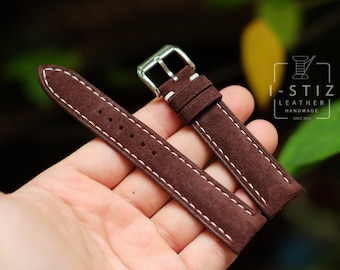 May include: A brown suede watch strap with white stitching. The strap has a silver buckle and is shown on a hand.