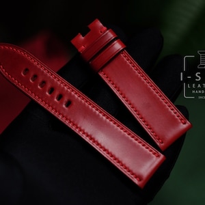 May include: Two red leather watch straps with white stitching. The straps are laid out on a black surface. The strap on the left has five holes for adjusting the size. The strap on the right has a more traditional design. The logo "I-STIZ LEATHER HANDMADE SINCE 2017" is visible in the upper right corner of the image.