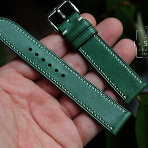 Könnte beinhalten: Grünes Leder-Uhrenarmband mit weißen Nähten und einer silbernen Schnalle. Das Armband ist handgefertigt und trägt den Text "I-STIZ LEATHER HANDMADE SINCE 2017".