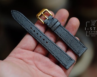 Könnte beinhalten: Ein schwarzes Lederarmband mit strukturierter Oberfläche und goldener Schließe. Das Armband wird auf einer Hand gezeigt.