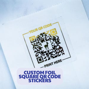 May include: White paper bag with a gold foil square QR code sticker. The sticker has a deer silhouette and the text "YOUR QR CODE" and "PRINT HERE". The bottom of the sticker reads "CUSTOM FOIL SQUARE QR CODE STICKERS".