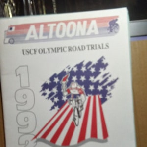 May include: A white program book with a red, white, and blue American flag design. The book is titled "Altoona USCF Olympic Road Trials 1992 & National Championships Official Program Book".