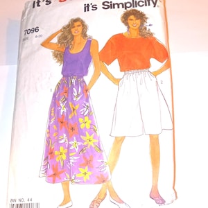 May include: A vintage Simplicity sewing pattern envelope. The cover features illustrations of two women wearing different outfits. One woman is in a purple top and floral skirt, the other in an orange top and white skirt. The text reads "It's so easy, it's Simplicity."