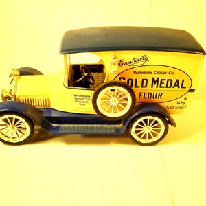 May include: A yellow toy delivery truck with blue accents, advertising "Washburn-Crosby Co. Gold Medal Flour". The truck has a white steering wheel and black tires.