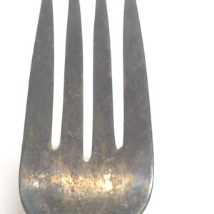 May include: A silver fork with an ornate handle. The fork has three tines and is slightly tarnished.