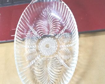 May include: A clear glass serving dish with a decorative pattern of leaves and circles. The dish has a scalloped edge and is oval shaped.
