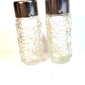 May include: A set of two clear glass salt and pepper shakers with silver tops. The shakers have a textured, diamond-like pattern.