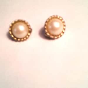 May include: A pair of gold-toned earrings with a pearl-like center. The earrings have a beaded edge.