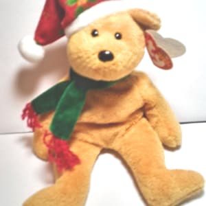 May include: A brown teddy bear wearing a red and green Santa hat with a green scarf. The bear has a black nose and brown eyes. The bear is sitting on a white background.