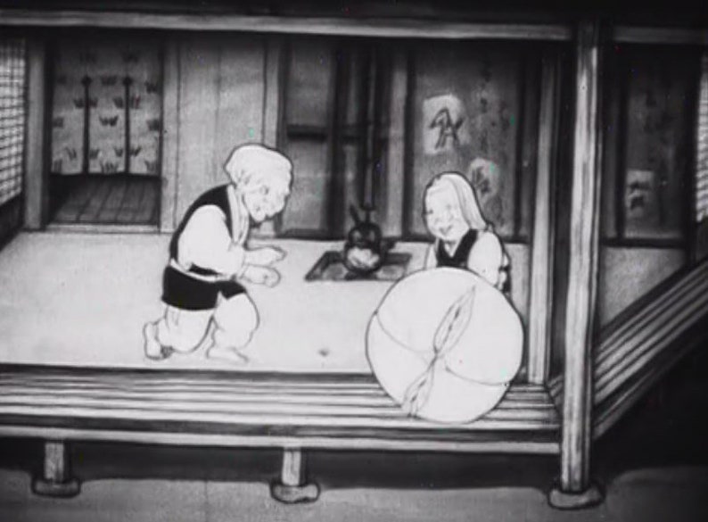 May include: A black and white image of two people in a room. The person on the left is wearing a long-sleeved shirt and pants. The person on the right is wearing a dress and holding a large, round object.