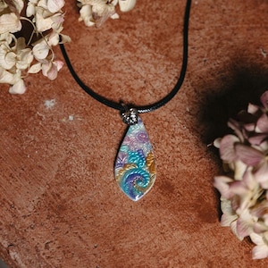 May include: A teardrop-shaped pendant necklace with a colorful, intricate design. The pendant features a swirling pattern of blue, purple, yellow, and white, with a silver-toned bail.