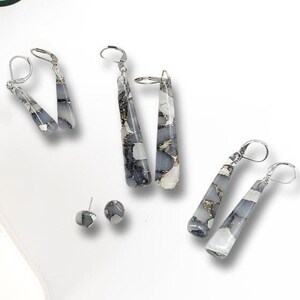 May include: A set of three pairs of dangle earrings with a gray and white marbled design. The earrings are made of metal and have a silver finish. The earrings are displayed on a white background.