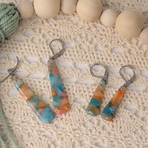 May include: A set of four colorful resin earrings with silver hooks. The earrings are made with a mix of blue, orange, and white resin.