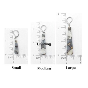 May include: Three pairs of silver dangle earrings with a long, teardrop-shaped stone. The stones are a white and gray color with black and gold flecks. The earrings are shown next to a ruler, with the smallest measuring 1 inch, the medium measuring 1.5 inches, and the largest measuring 2 inches.