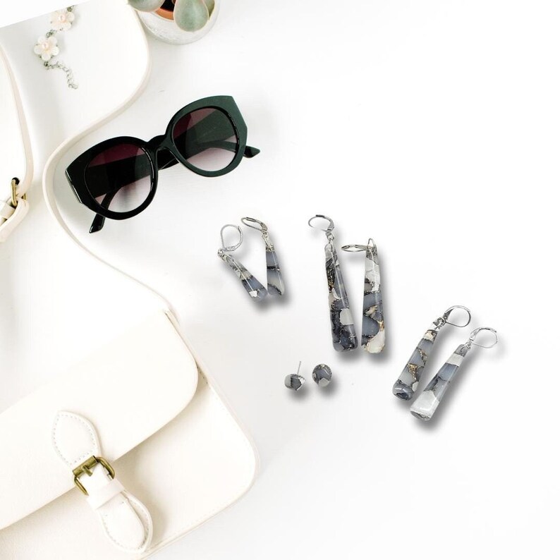 May include: A set of three pairs of dangle earrings with a gray and white marbled design. The earrings are made of metal and have a silver finish. The earrings are displayed on a white background.