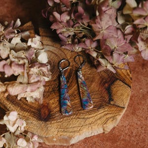 May include: A pair of dangle earrings with a geometric design. The earrings are made of a colorful, iridescent material and have silver hooks.