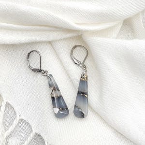 May include: A pair of silver dangle earrings with gray and white striped resin teardrop-shaped pendants with gold flecks.