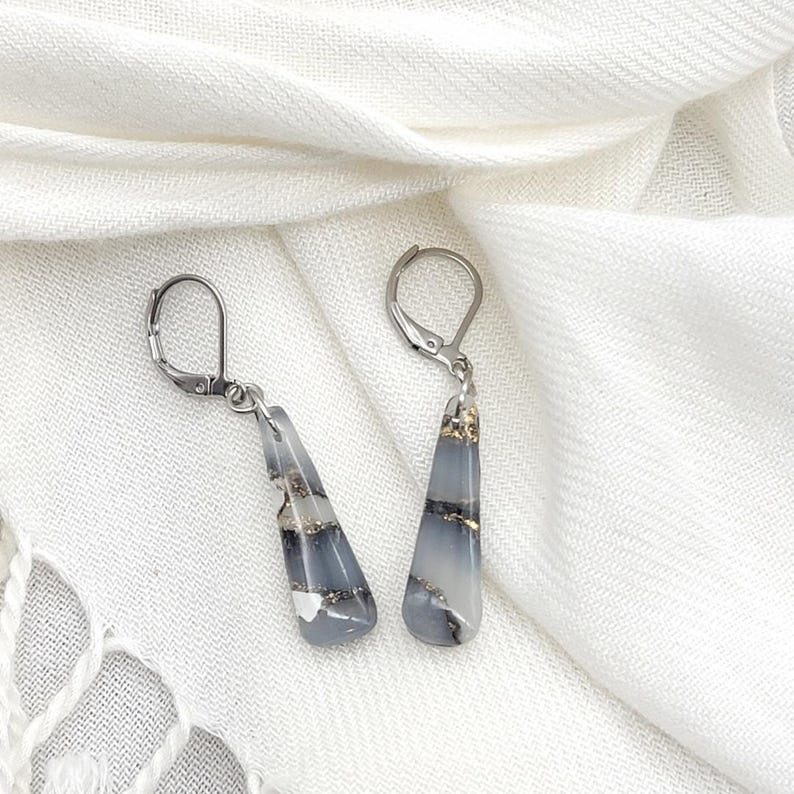 May include: A pair of silver dangle earrings with gray and white striped resin teardrop-shaped pendants with gold flecks.