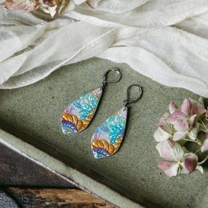 May include: A pair of teardrop-shaped earrings with a colorful floral pattern. The earrings are made of polymer clay and have silver hooks.