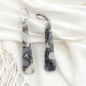 May include: A pair of long, silver dangle earrings with a white and gray stone pendant. The stone has a marbled pattern with gold flecks.
