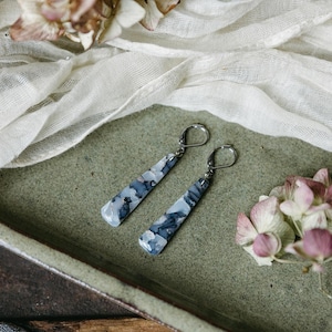 May include: A pair of silver dangle earrings with long, rectangular, blue and white marbled stone drops.