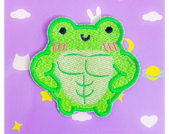 Könnte beinhalten: Grüner gestickter Bügelaufkleber mit einer Cartoon-Frosch mit prallen Muskeln. Der Frosch lächelt und hat rosa Wangen. Der Aufkleber befindet sich auf einem violetten Hintergrund mit weißen Wolken und Sternen. Der Text "momokakkoii.com" befindet sich am unteren Rand des Bildes.
