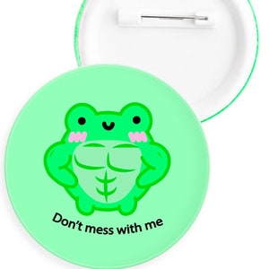 Pode incluir: Botão verde com uma imagem de desenho animado de um sapo verde com bochechas cor-de-rosa flexionando seus músculos. O texto "Don't mess with me" está impresso abaixo do sapo.