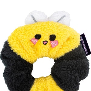 May include: A yellow and black fuzzy bee-shaped hair scrunchie with a cute embroidered face and the text "momokakkoi" on the side.