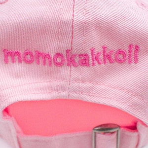 Puede incluir: Gorra de b&eacute;isbol rosa con un logotipo bordado que dice "momokakkoli" en hilo rosa.