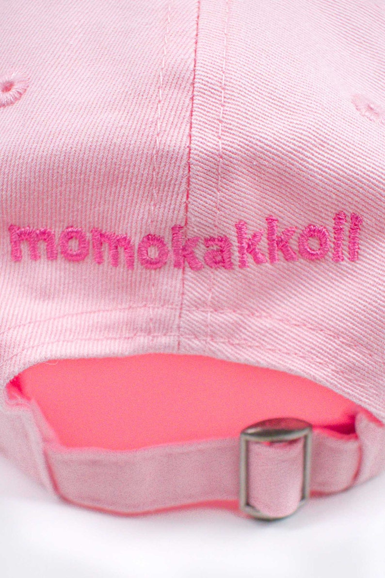 Puede incluir: Gorra de b&eacute;isbol rosa con un logotipo bordado que dice "momokakkoli" en hilo rosa.