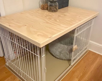 May include: A white metal dog crate with a wooden top. The crate has a door on the side and a gray bed inside.